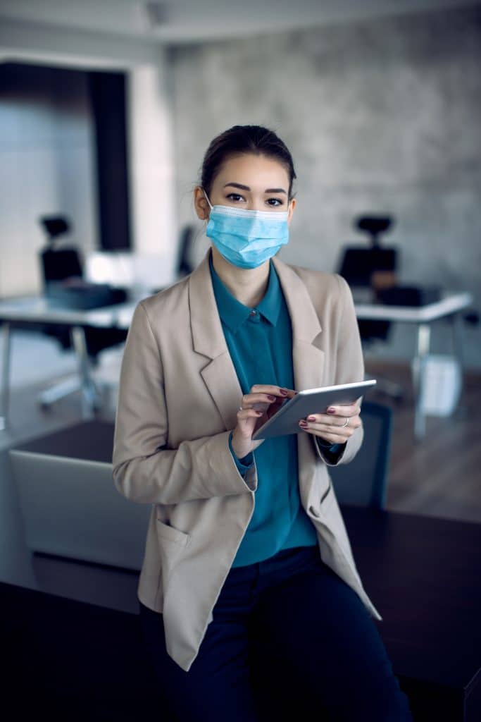 Female entrepreneur with face mask working on digital tablet in