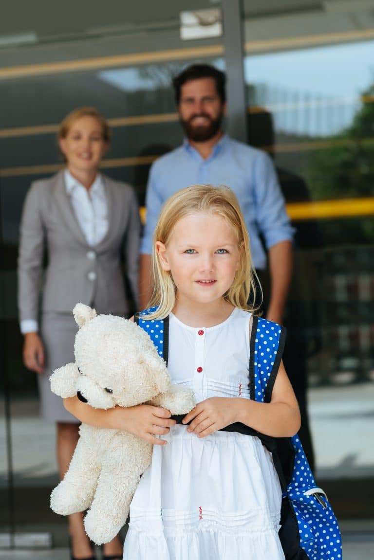 Portrait of lovely little schoolgirl with a teddy bear and her smiling parents in background